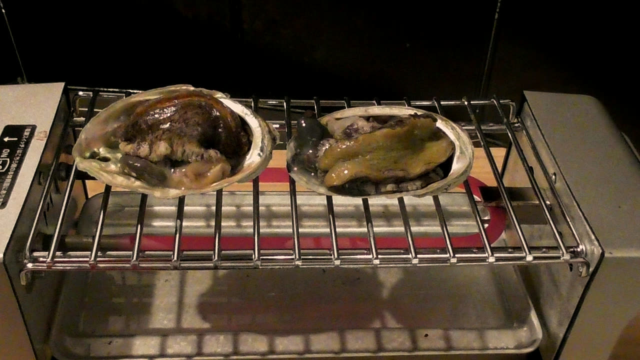 網の上で、熱で身をくねらせる鮑2個