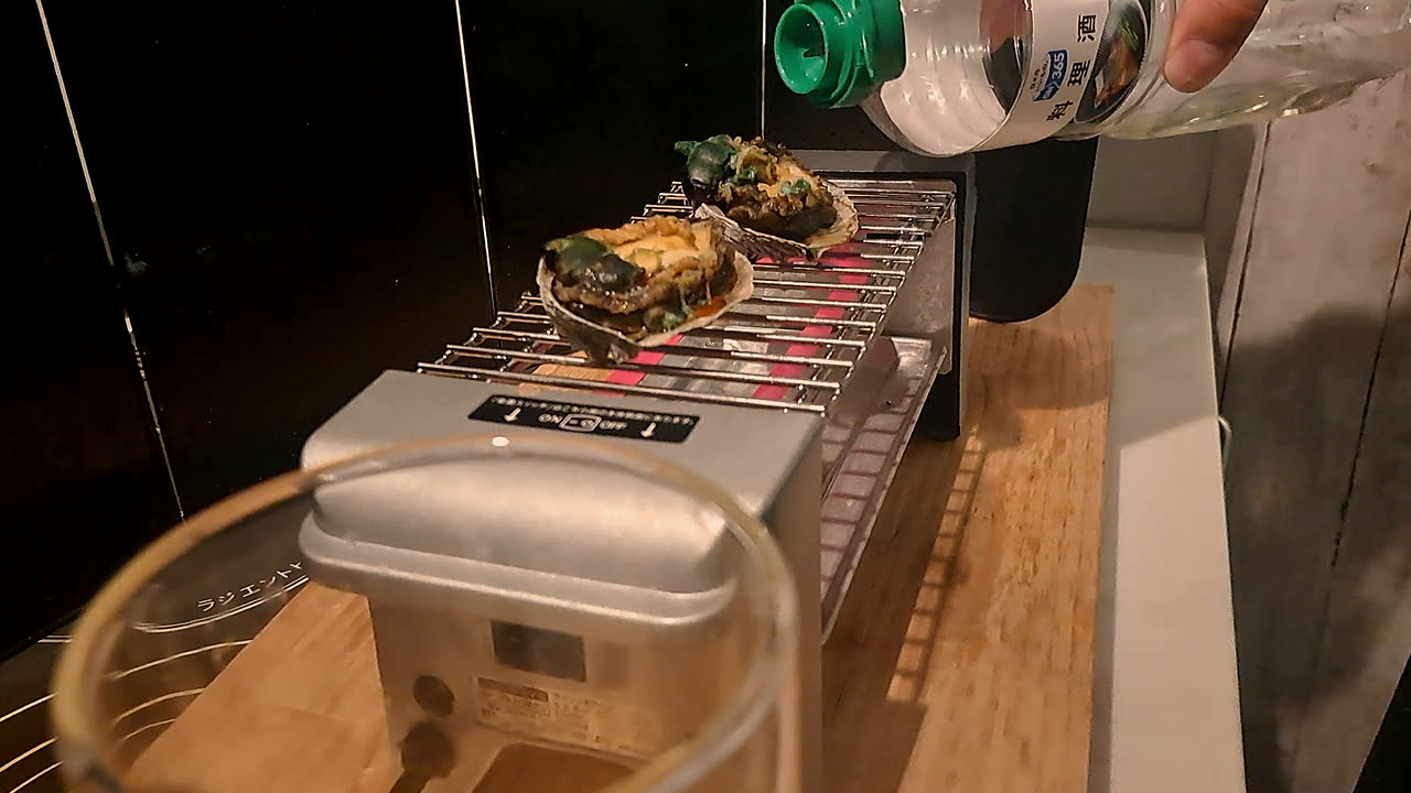 網の上の鮑に、料理酒を注いでいるところ