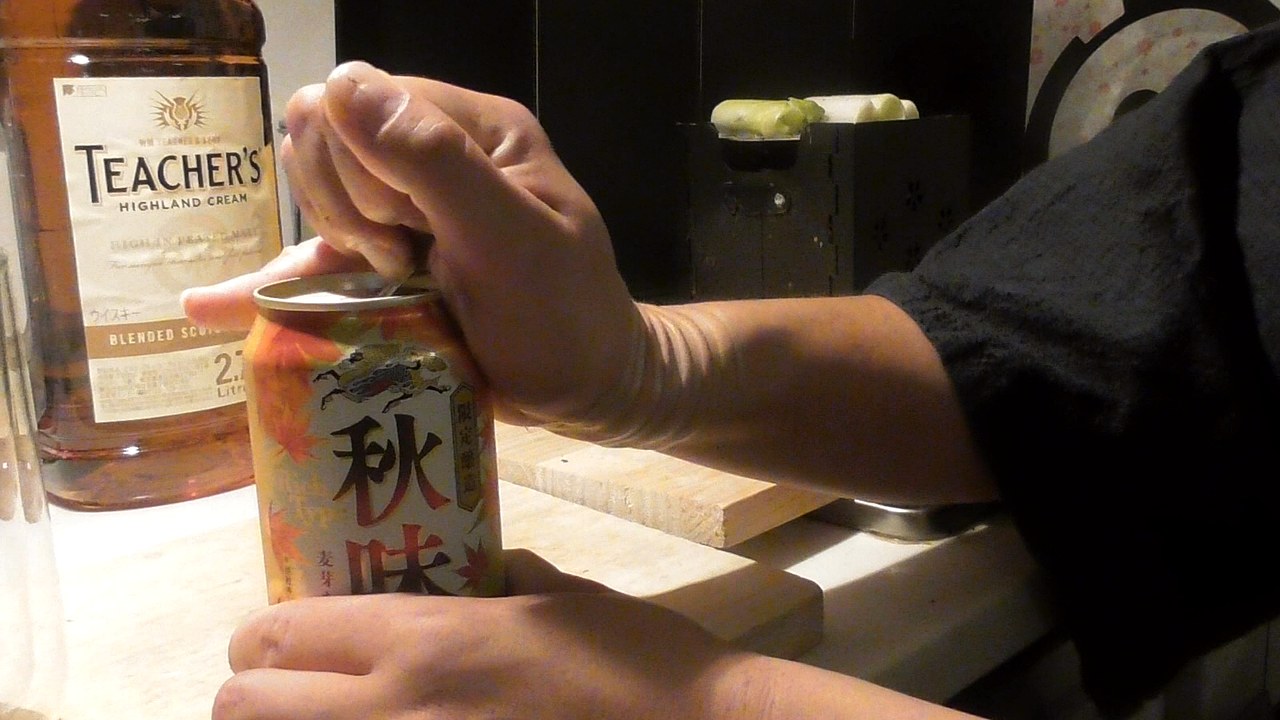キリン秋味の缶をあけているところ。うしろにティーチャーズのボトルと、網の上で焼いている長ネギ