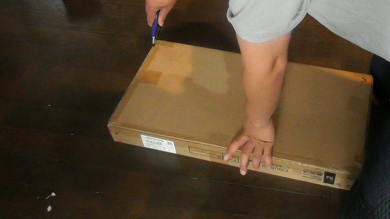 床に置いたカラボの箱のテープを、カッターで切って開けているところ