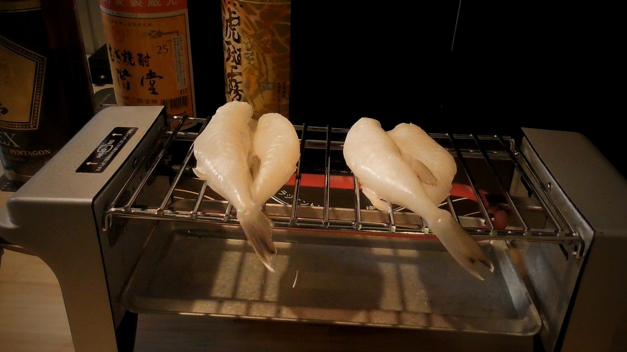 焼き鳥グリルの網にのった2枚のふぐの一夜干しのアップ。まだ真っ白で焼き色がない