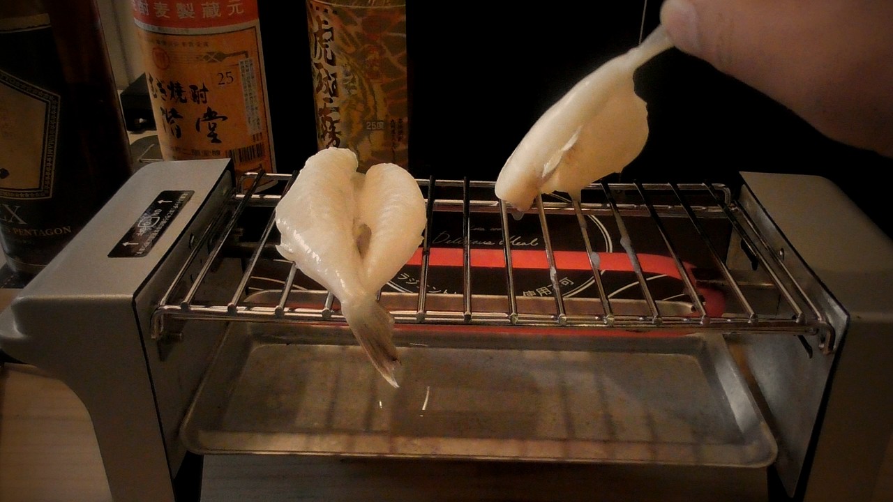 網の上の右のふぐの尾を指でつまんで持ち上げ、裏返そうとしているところ。持ち上げた面も白い