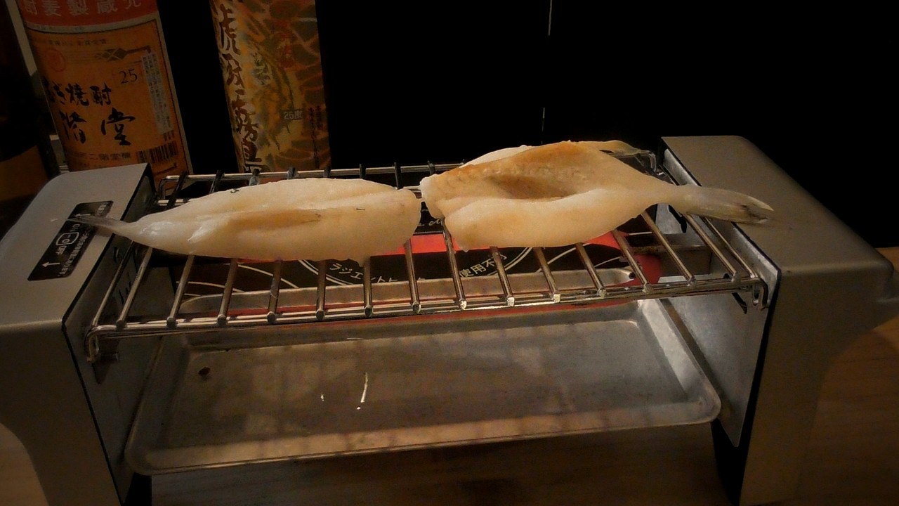 網に横向きに寝かせたふぐの一夜干し2枚。右の1枚に茶色い焼き色がついている
