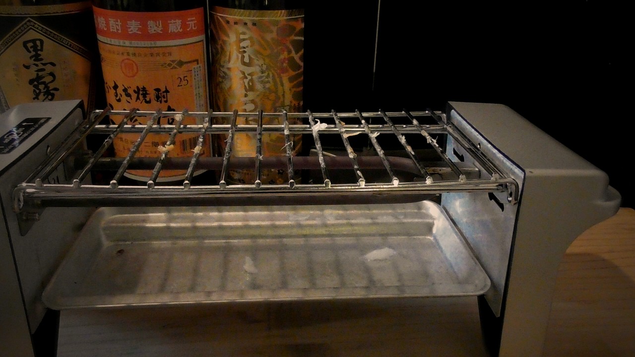 食べ終わって空になった焼き鳥グリルの網。網と受け皿に白い身のかけらが少し残っている。奥に焼酎のビン