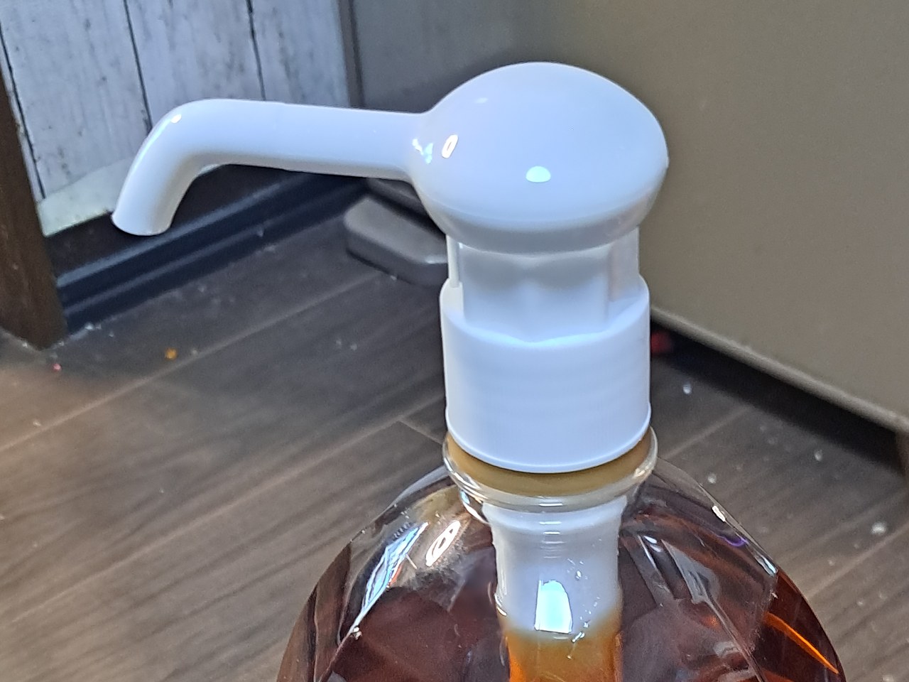 トリスの4Lペットボトルの口に付いた、白いポンプの頭のアップ。丸い頭から左へ注ぎ口がのびている。下にボトルの口と、中へ下りていくチューブ