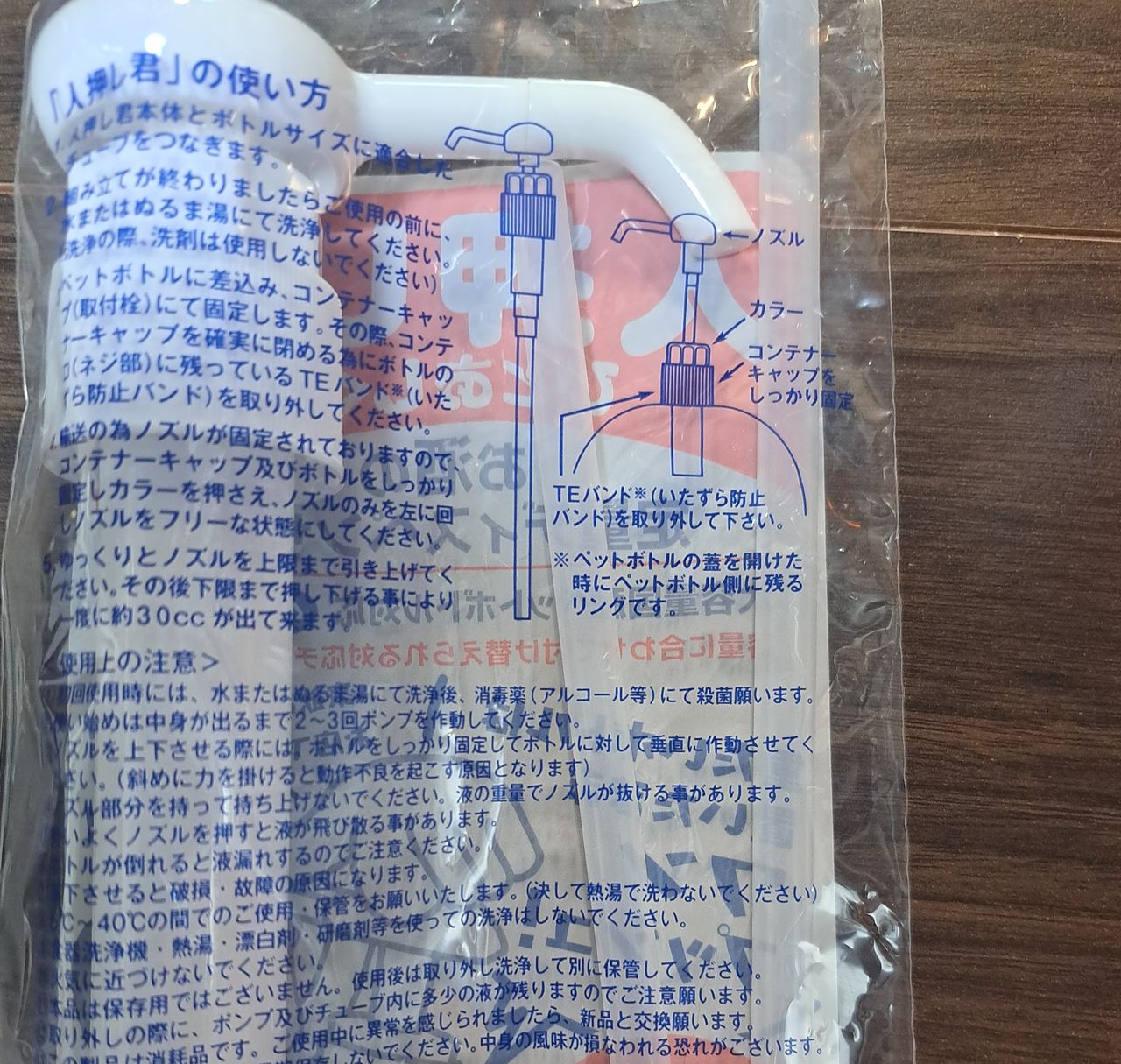 袋の裏の「『人押し君』の使い方」。青い文字の説明が並び、右にポンプを取り付けるときの図。ノズル、カラー、コンテナーキャップの名前と、「TEバンド（いたずら防止バンド）を取り外して下さい」の説明。下に「使用上の注意」の文が続く