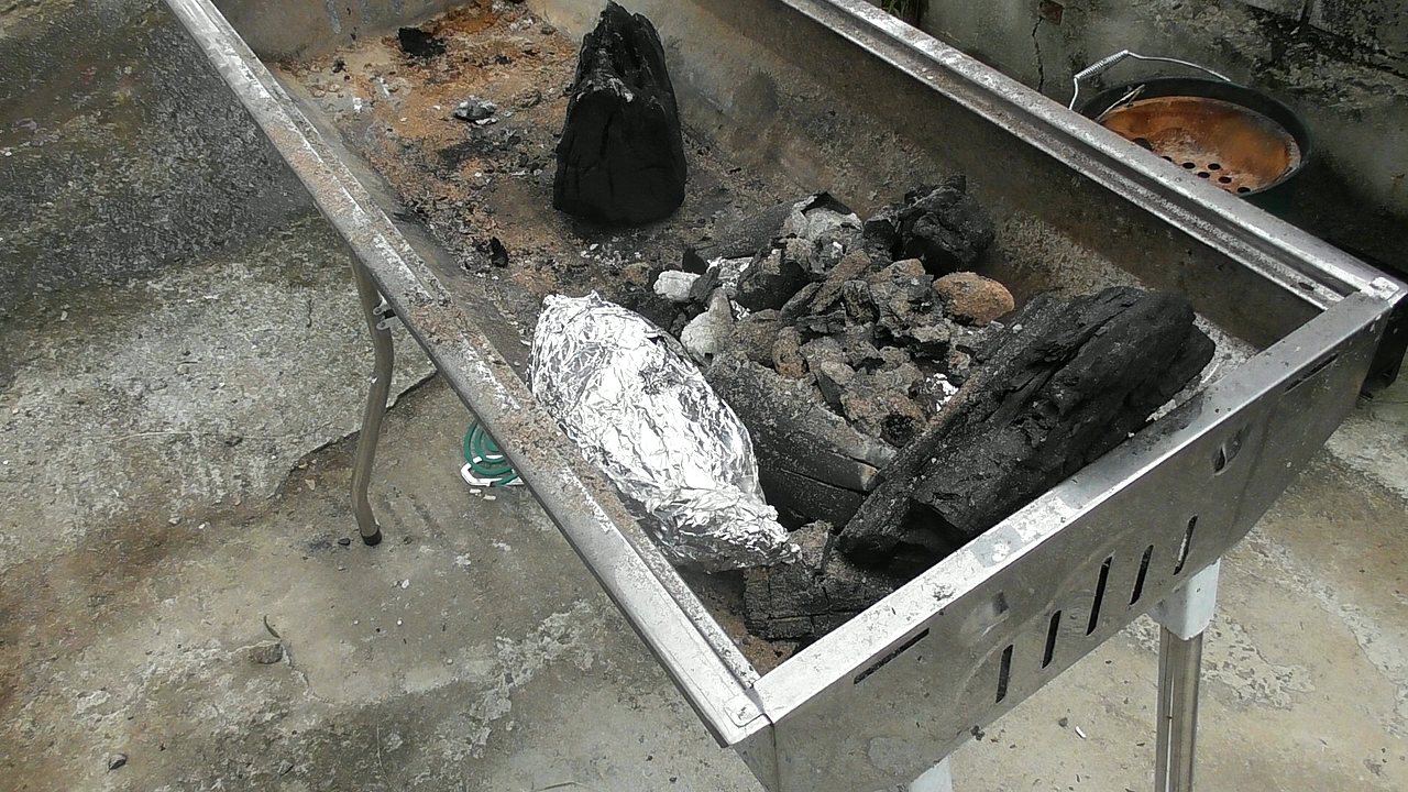 大きいバーベキューコンロの炭の中に、アルミホイルで包んださつまいもが入っている