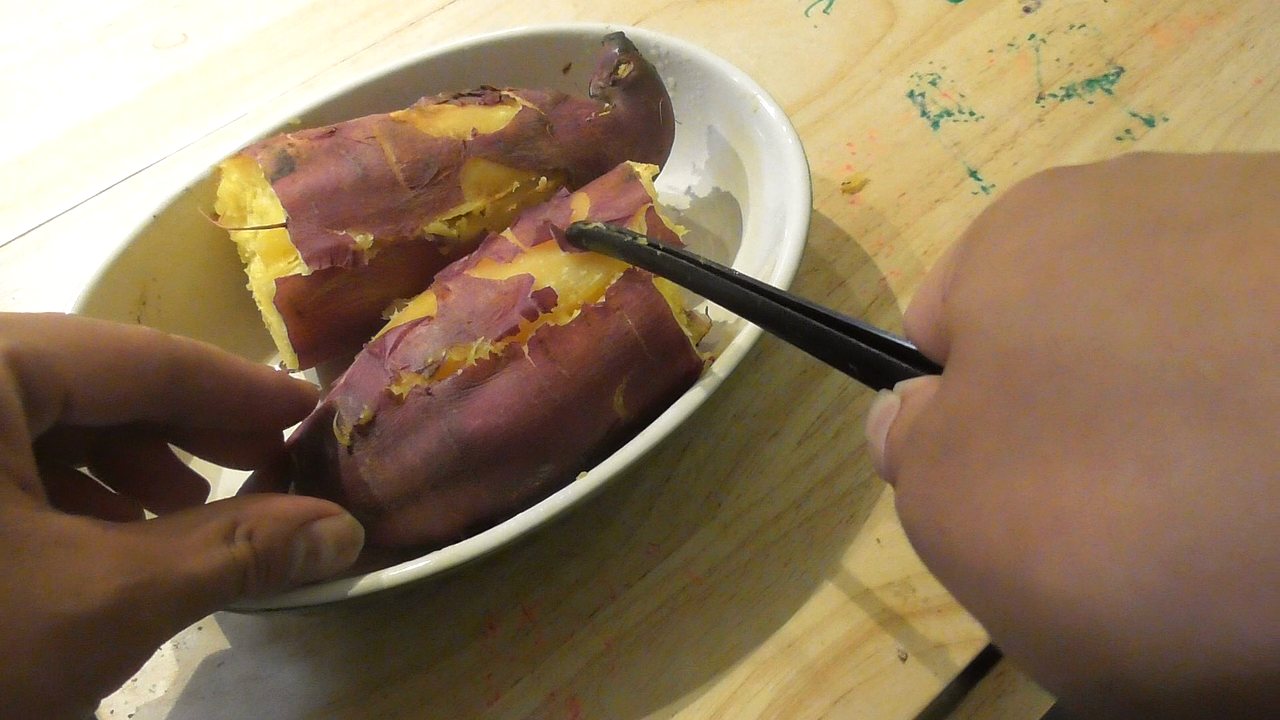 皿の上の2つに割った焼き芋を、トングで切ろうとしているところ